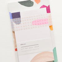 Brights Multi: Two stacked notepads wrapped with cellophane, decorated with colorful abstract shapes.