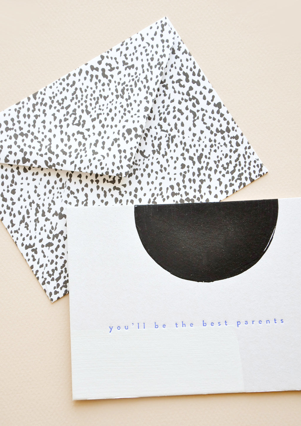 2: A black and white dotted envelope and white greeting card with a black semicircle and the text "you'll be the best parents" in blue.