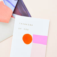 2: Painted shapes in shades of pink on white greeting card with words "Thinking Of You" in gold foil. Shown with envelope painted with abstract lines.