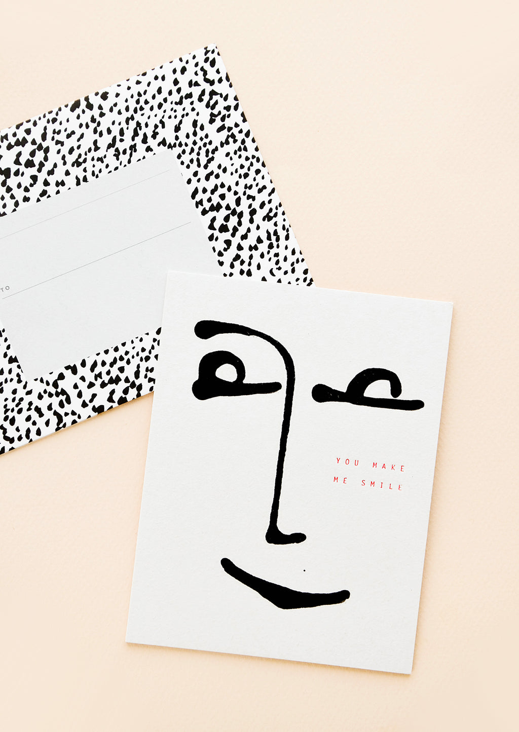1: A black and white polka dot envelope and a white greeting card with a minimalist image of a smiling face.