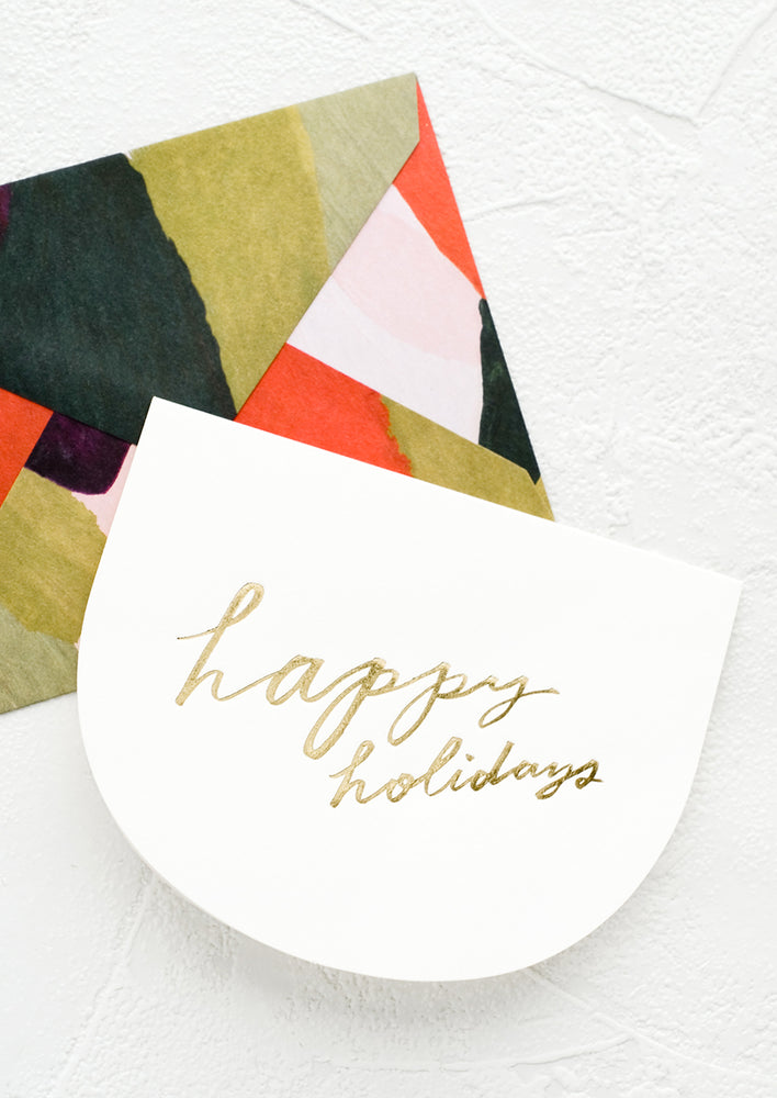 1: Greeting card in curved shape with gold script reading "Happy holidays", paired with green and red abstract envelope.