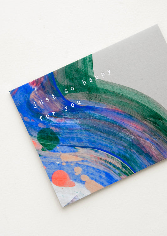 Greeting card with painted streaks of color in earth tone hues, white lettering reads "Just so happy for you"
