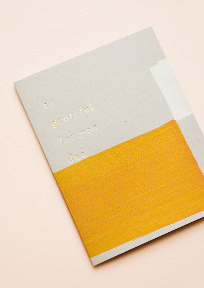Greeting card with hand-painted square shapes in mustard and white, gold text reads "So grateful for you dad"