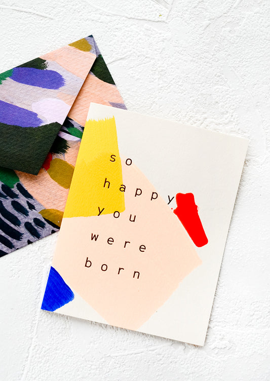 A greeting card with hand-painted geometric shapes and text reading "So happy you were born"
