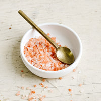 2: A brass spoon inside a small white dish with coarse pink salt.