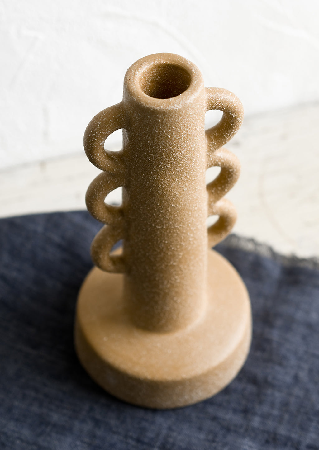 3: A textured sand colored taper holder with decorative loop shape.