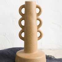1: A textured sand colored taper holder with decorative loop shape.