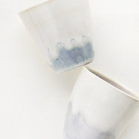 2: Two small ceramic cups in drippy ivory and grey-blue glaze.