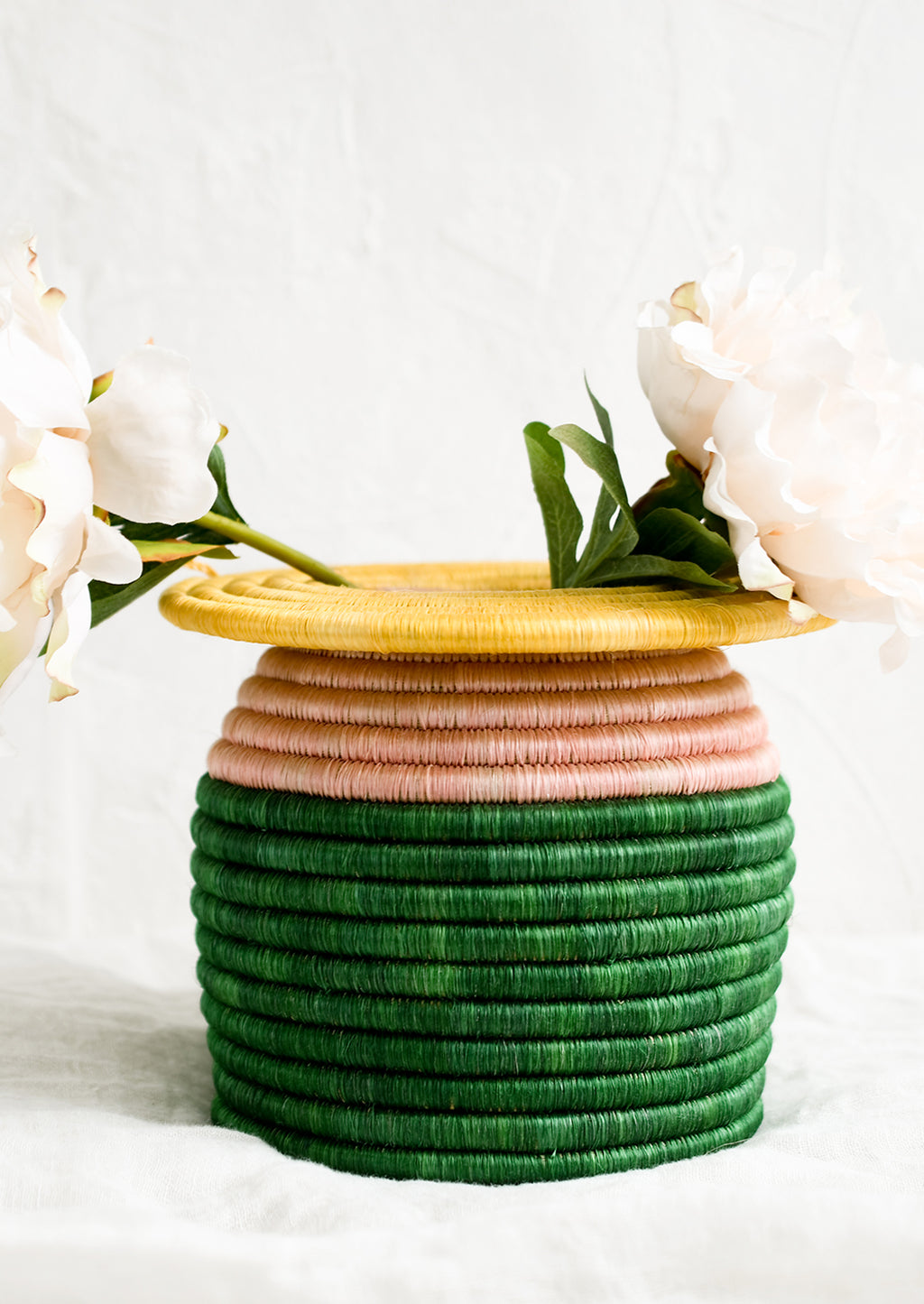 1: A color blocked, woven sweetgrass vase with peonies.