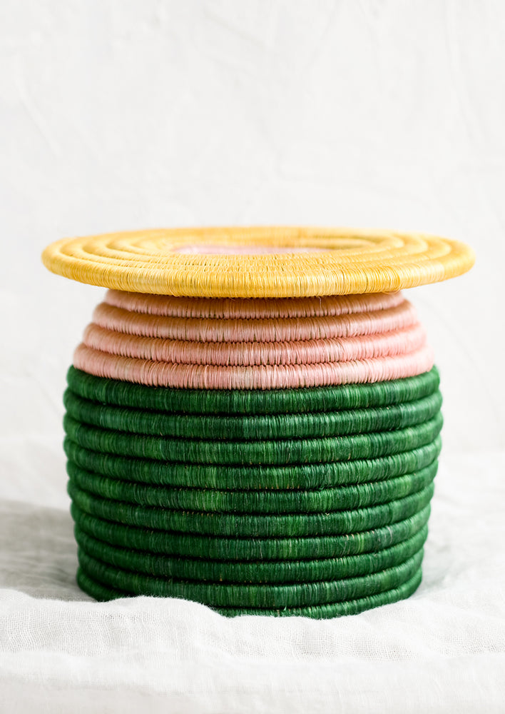 A color blocked, woven sweetgrass vase with flat top in yellow, pink and green.