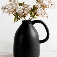 1: A black ceramic vase in jug shape, holding flowers.