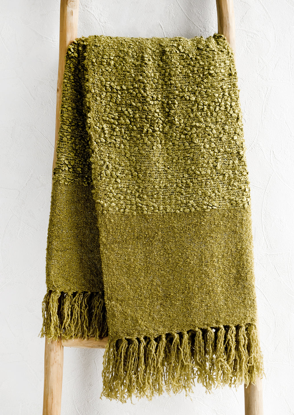 1: A moss green boucle throw with tassel trim.