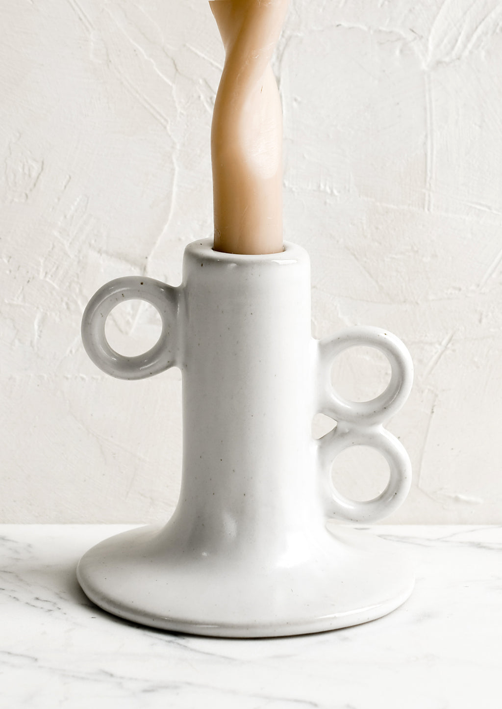 2: A sculptural taper candle holder in white ceramic with beige candle.