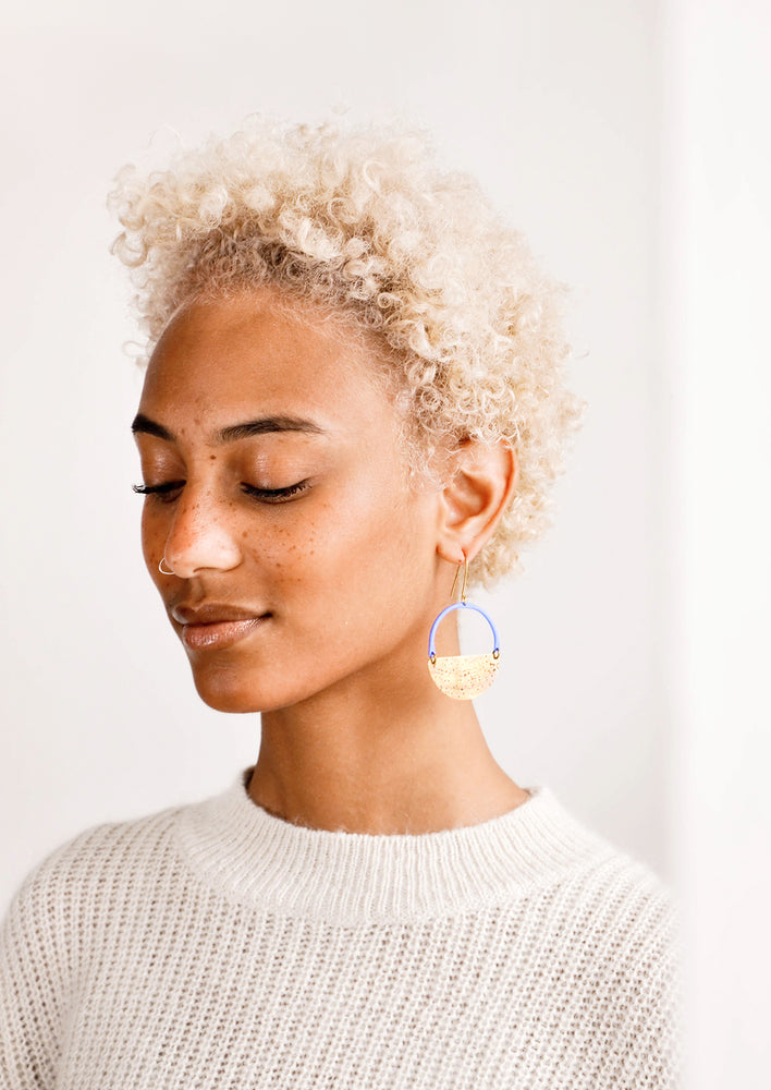 Model wearing blue and brass circular earrings