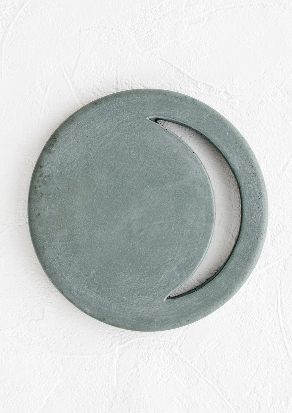 Petrol: A round concrete trivet in marine color with crescent moon shaped cutout.