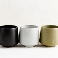 2: A row of three ceramic cups in black, white and olive.