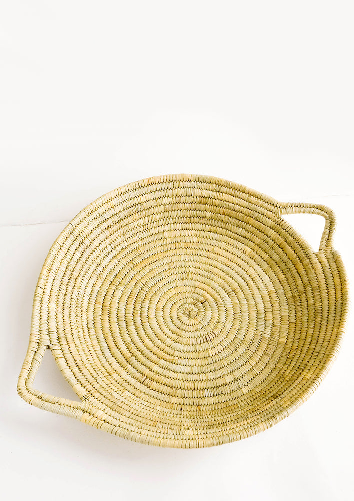1: Flat, round platter woven from natural straw with handles at sides