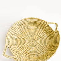 1: Flat, round platter woven from natural straw with handles at sides