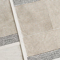 Taupe / Deep Indigo: A cotton placemat with block print design, borders at top and bottom with striped center.