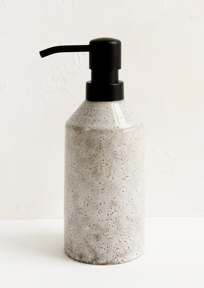 A ceramic soap dispenser in speckled tan with black hardware.