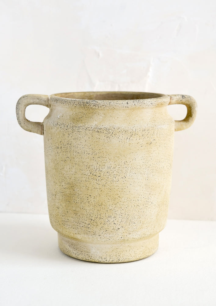 A distressed beige ceramic vase with handles at top sides.