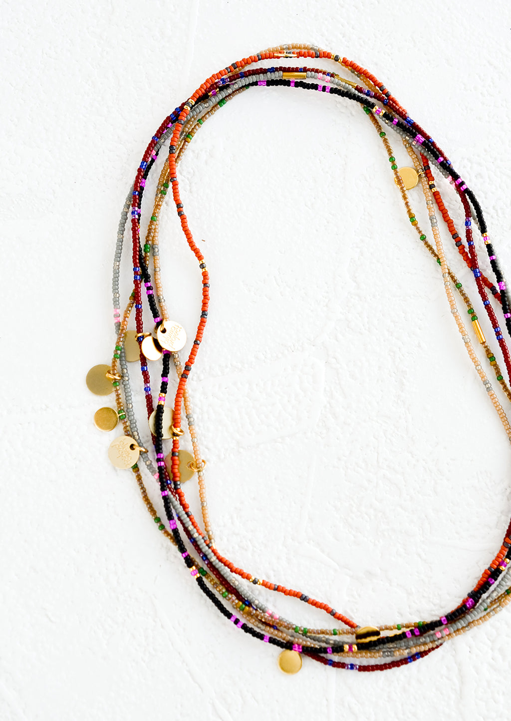 2: A layered, stacked pile of seed bead choker necklaces with brass charm details.