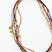2: A layered, stacked pile of seed bead choker necklaces with brass charm details.