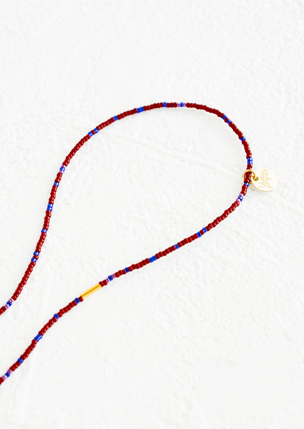 Wine / Cobalt: A strand of seed beads in burgundy and blue with brass charm details.