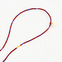 Wine / Cobalt: A strand of seed beads in burgundy and blue with brass charm details.