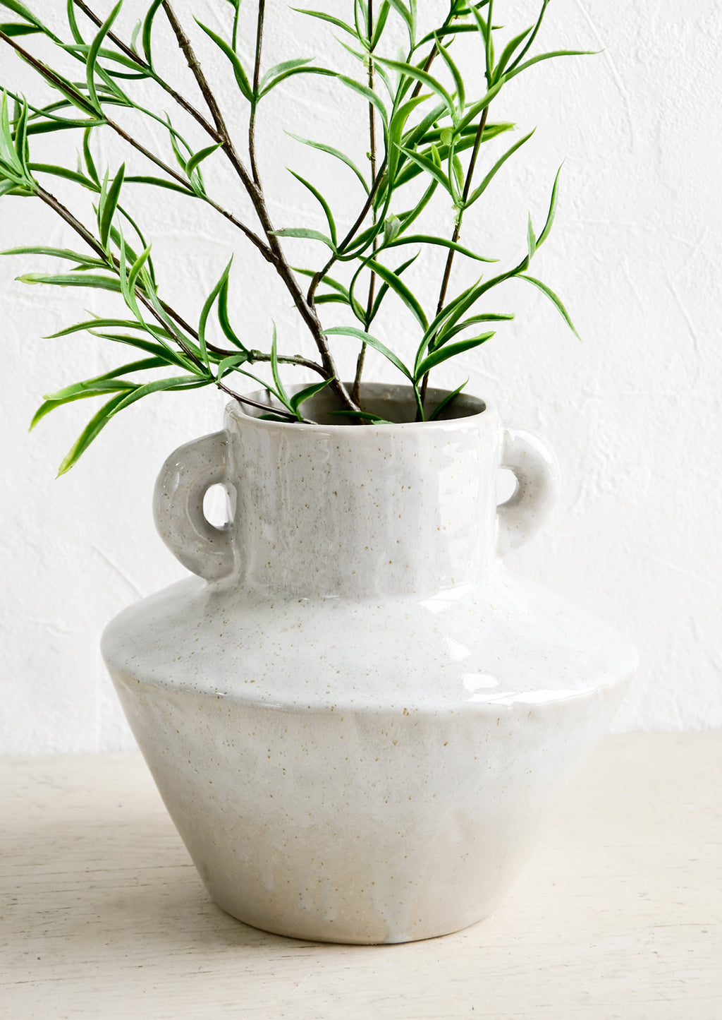 1: Grey ceramic vase in askew silhouette with green leaved branches.