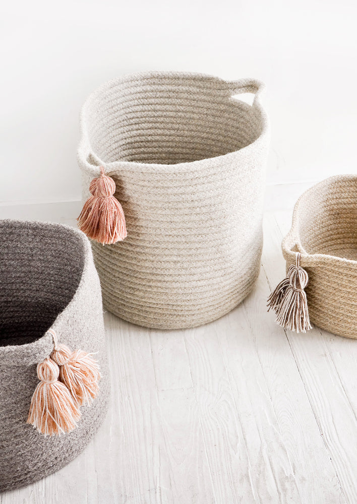 2: Round storage bins in natural wool. Handles at sides with oversized tassel detail.