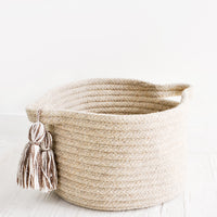 Small / Oatmeal: Round, low storage bin in natural wool. Handles at sides with oversized tassel detail.