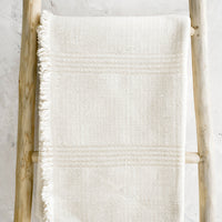 1: Woven throw made from natural undyed cotton with textural tonal stripes and fringed trim on one side