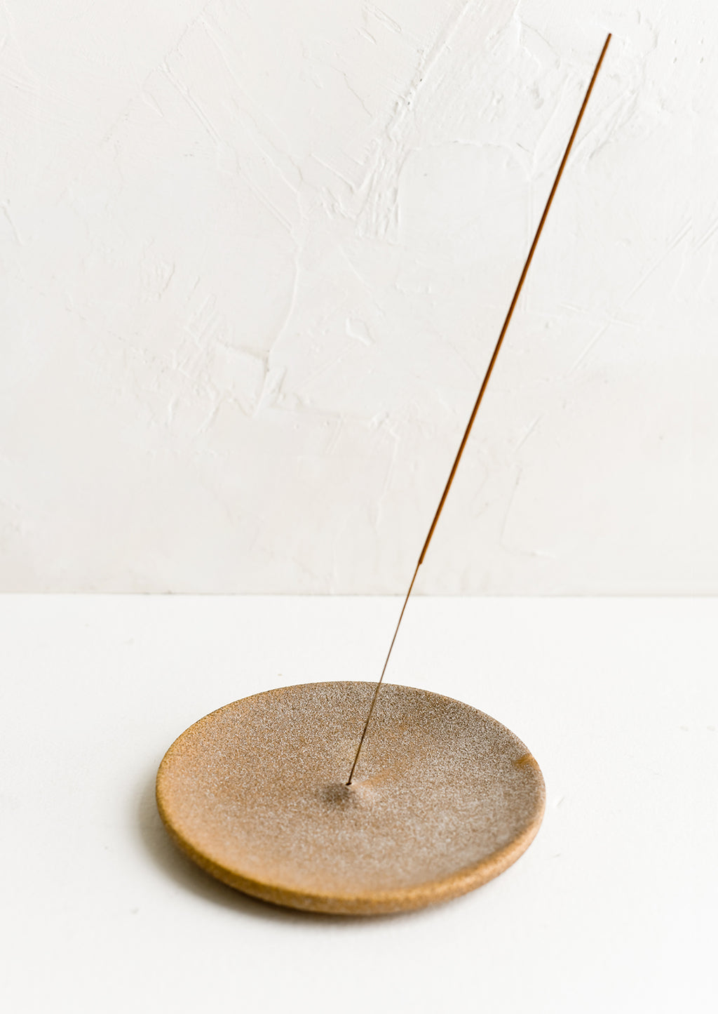 2: A sandy brown ceramic incense holder holding incense stick.