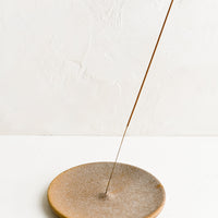 2: A sandy brown ceramic incense holder holding incense stick.