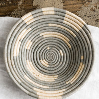 1: A round raffia bowl in dusty blue-grey and natural spiral geometric pattern.
