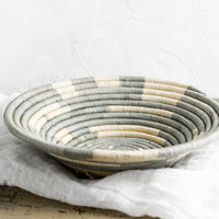 2: A round raffia bowl in dusty blue-grey and natural spiral geometric pattern.