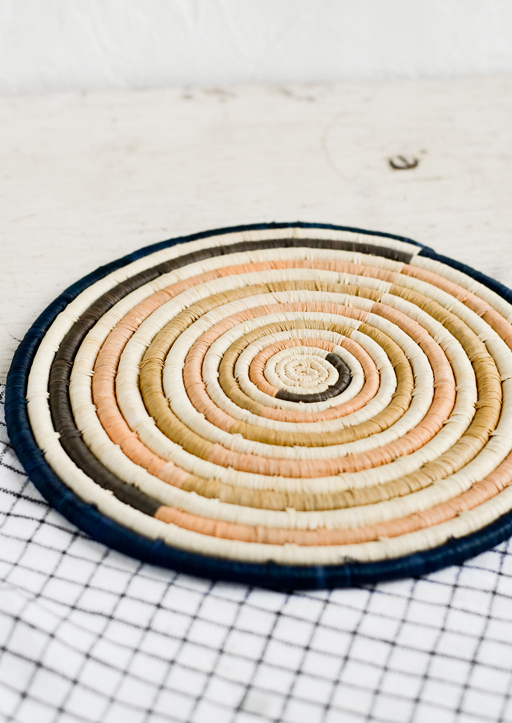 Peach / Navy Multi: A round natural fiber trivet in peach and navy colorblock design.