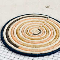 Peach / Navy Multi: A round natural fiber trivet in peach and navy colorblock design.