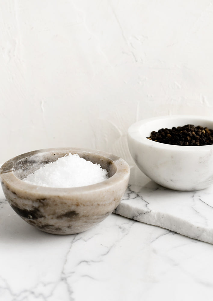 Tan and white marble bowls holding salt and pepper.