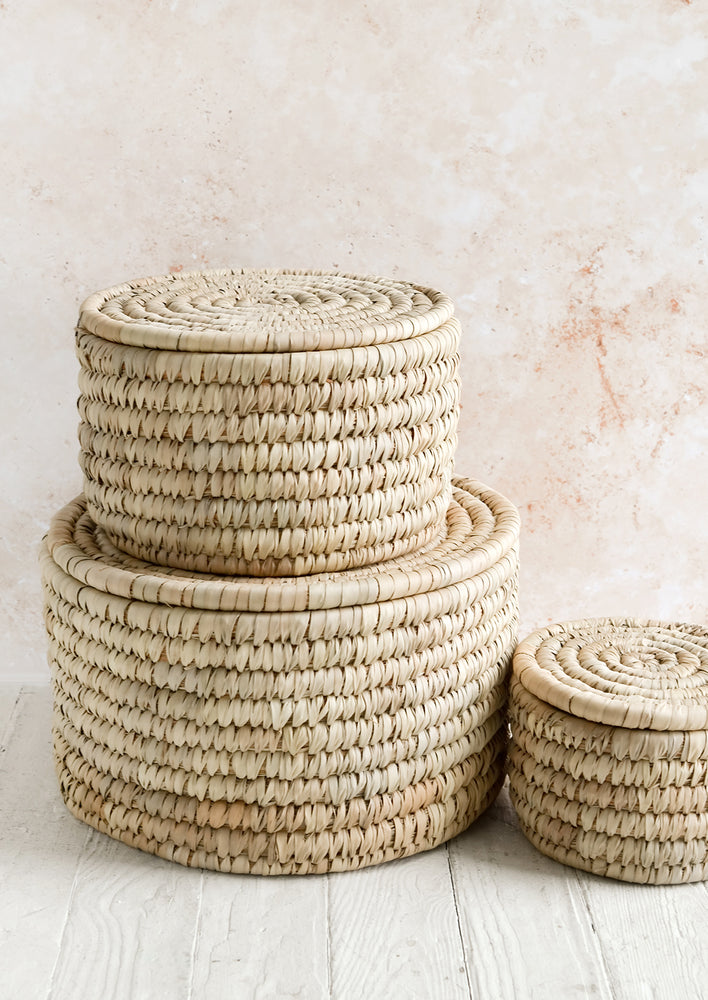 Three round, palm leaf storage baskets with lids in incremental sizes.