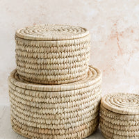 2: Three round, palm leaf storage baskets with lids in incremental sizes.