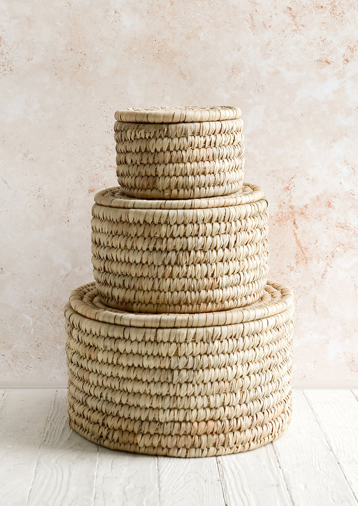 1: Three round, palm leaf storage baskets with lids in incremental sizes.