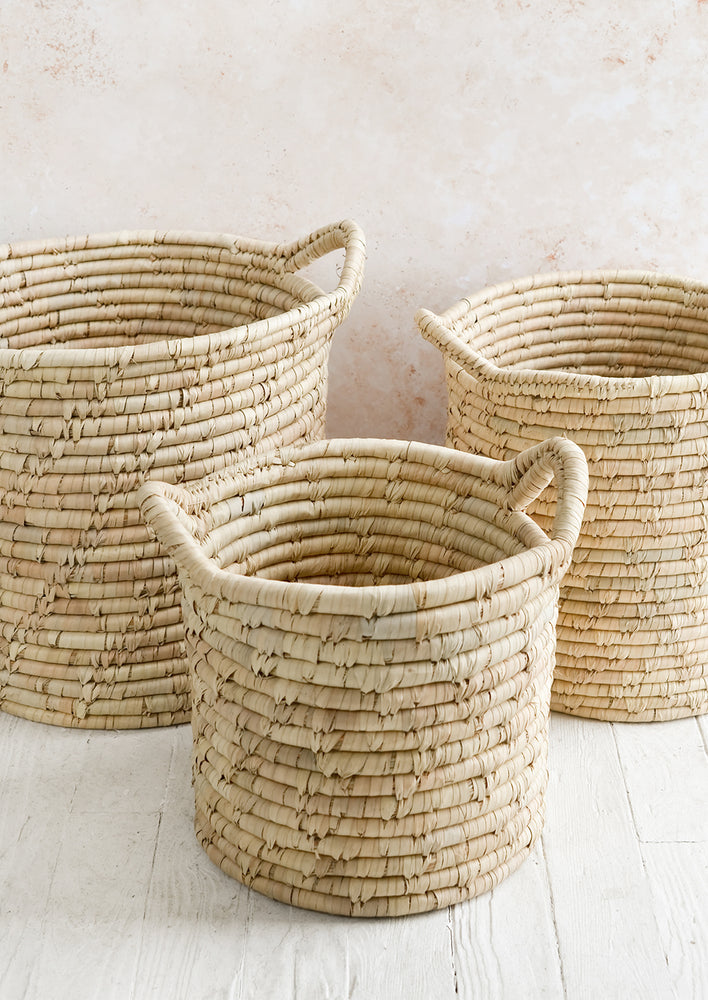 Three round, open-top storage bins woven from natural palm leaf, shown in three incremental sizes.