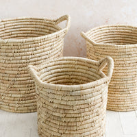 2: Three round, open-top storage bins woven from natural palm leaf, shown in three incremental sizes.