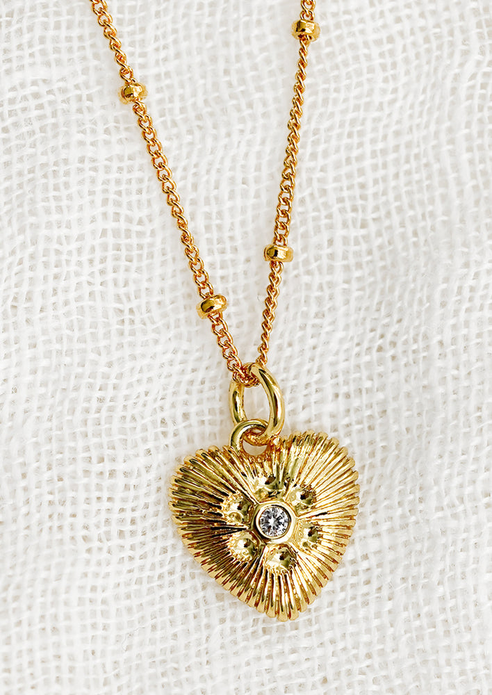 1: A gold necklace with heart shaped charm with ridged texture and crystal detailing.