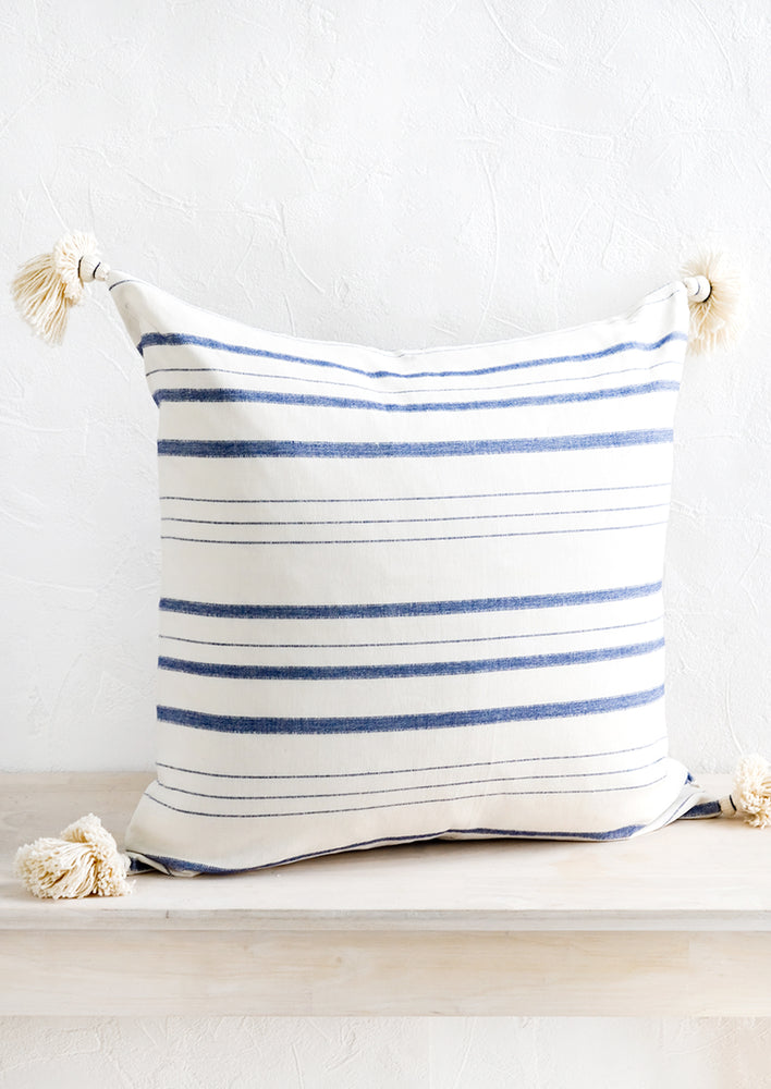 1: A square throw pillow in white cotton with horizontal blue stripes and tassels at corners.