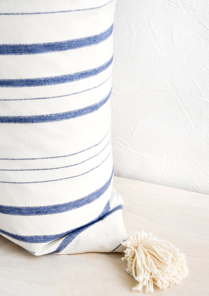 A striped throw pillow in white & blue with cream-colored yarn tassel at corner.