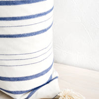2: A striped throw pillow in white & blue with cream-colored yarn tassel at corner.