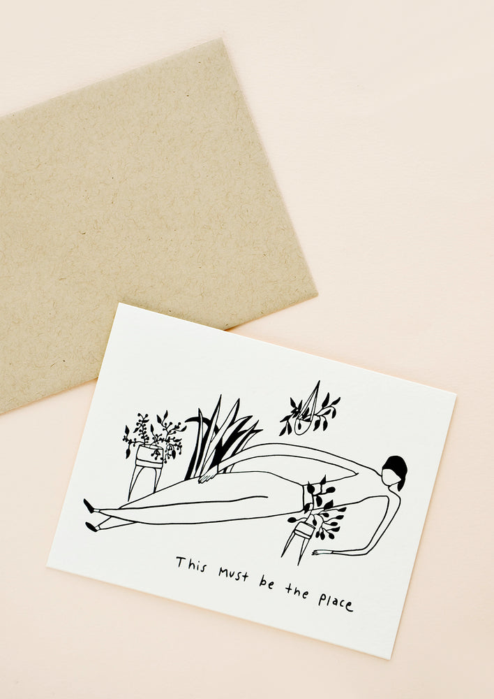 Greeting card with illustration of woman lying down, surrounded by potted plants, with the text "this must be the place" at bottom
